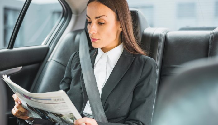 beautiful-young-businesswoman-traveling-by-car-reading-newspaper